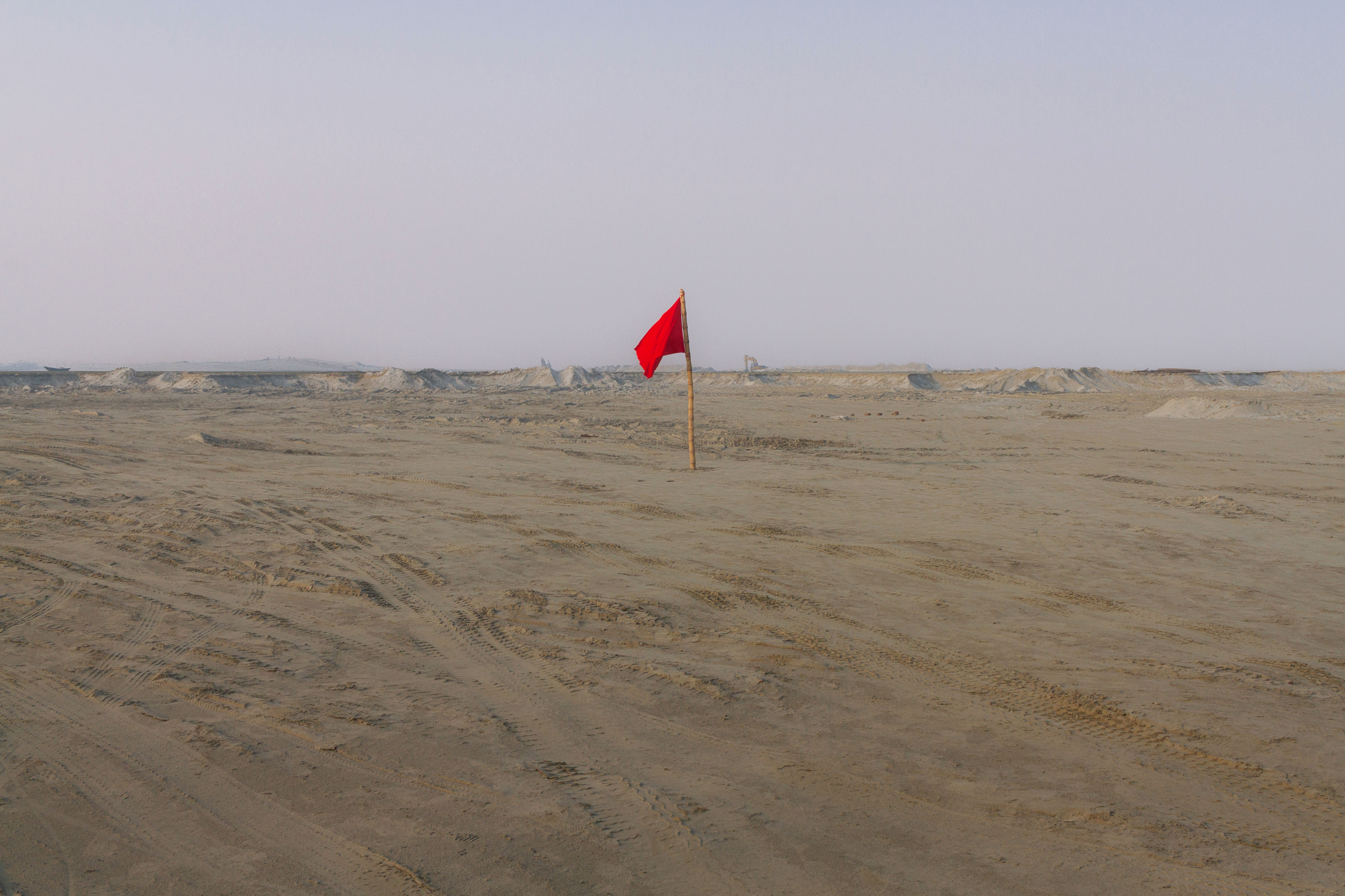 A lone red flag whispers to the wind, a silent sentinel in the endless sand. Does it mark a warning, or a forgotten promise? Only the shifting dunes will know.